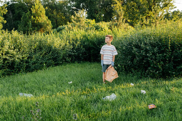 A seven-year-old boy at sunset is engaged in garbage collection in the park. Environmental care,...