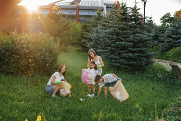 A group of adults and children together at sunset is engaged in garbage collection in the park....