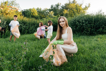 A group of adults and children together at sunset is engaged in garbage collection in the park....
