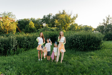 Obraz premium A group of adults and children together at sunset is engaged in garbage collection in the park. Environmental care, waste recycling. Sorting garbage.