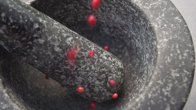 Close-up of the red peppercorns are falling into the grey stone mortar