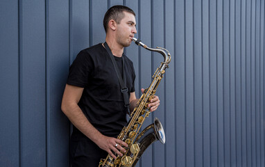 Fototapeta na wymiar Young street musician playing saxophone near the big blue wall