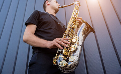 Young street musician playing saxophone near the big blue wall
