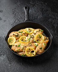 Chicken Piccata with capers, white wine sauce in iron cast pan. Italian food
