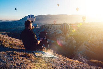 Male tourist with laptop looking at hot air balloons