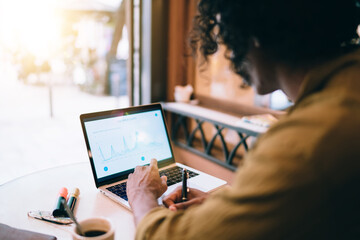 Anonymous ethnic man taking notes in cafe