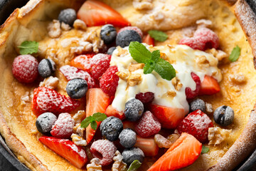 Dutch baby pancake with berries and icing sugar in a iron cast pan. Morning breakfast