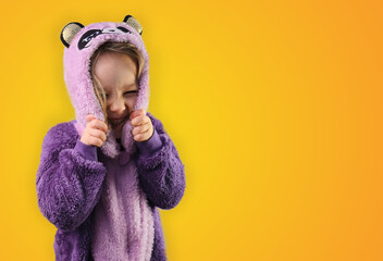 Little girl toddler child wear hooded purple pajamas smiling on isolated yellow 