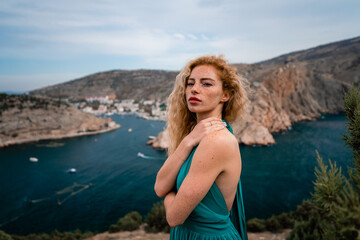 Obraz premium A woman in an emerald dress, a fashion model with long silk wings in a flowing dress, flying fabric on the embankment.
