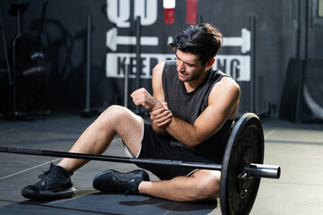 Fototapeta na wymiar Young Caucasian men grab his arm and wrist and feeling painful while weight lifting exercise inside of sport gym. Sport accident, overtrain
