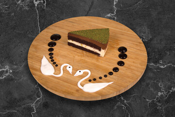 Homemade layered pistachio dark chocolate raw vegan cake slice on wooden plate with nut green piece texture