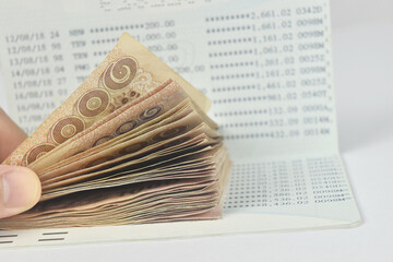 Hand with thai money and bank saving account book on white background.