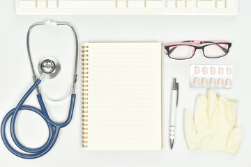 Blank notebook with stethoscope, glasses, medical glove on doctor desk.