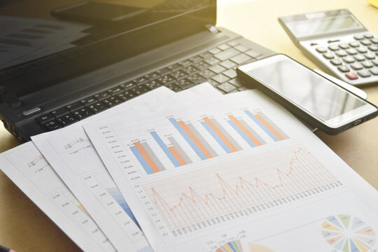 Financial graphs and charts with laptop, smartphone, calculator and pen on desk.