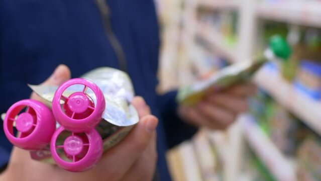 Shopping in the store, a man holds in his hands airtight packages of food in tubes with pink lids. Selection of food in the supermarket. Buying non-perishable food at the store for stock.
