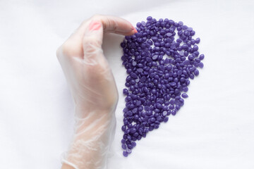 a gloved hand and depilation wax in the form of a heart. The concept of sugaring