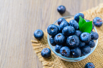 Fresh organic blueberries in a glass bowl on wood background,