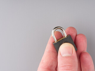 A small lock in his hand on a gray background. Closeup. Space for text