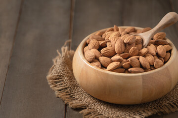 Almonds nut and wood spoon  in wood cup on wood background.
