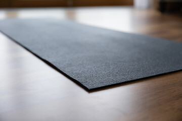 Black rubber yoga mat on floor inside domestic room or class sport club space. Sportive exercise at home or gym, healthy active lifestyle, personal accessory for comfort work out. Training concept