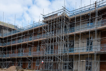 New residential multistorey apartment building made of brick and concrete block, with scaffolds erected around it to provide access for external works, with retaining wall and pre-cast stairs  