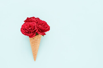 Red roses in ice-cream cone on a light blue background. Summer concept. Copy space