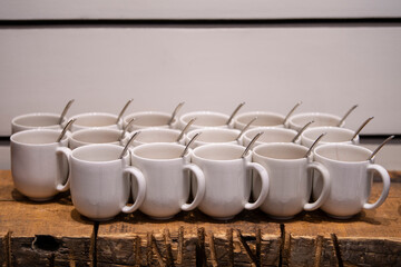 Row of white ceramic coffee or tea cups with spoons on wooden table. Coffee break for seminar audience, or conference event in meeting room.