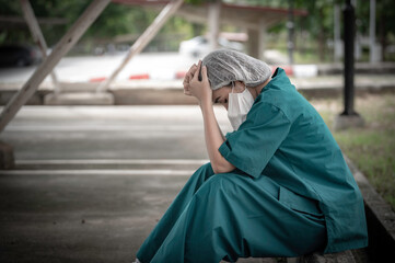 Tired depressed female asian scrub nurse wears face mask blue uniform sits on hospital floor,Young woman doctor stressed from hard work