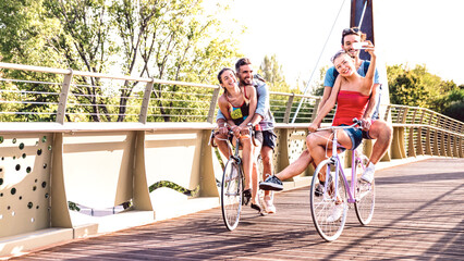 Young milenial friends having fun riding bike at city park bridge - Life style concept with happy...