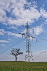 A High voltage pole with blue white sky and a tree