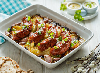 Baked white sausage with the addition of onion, garlic and herbs in a baking dish, close-up view....