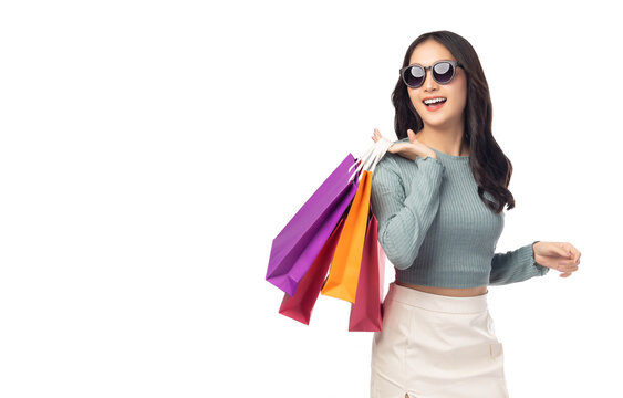 Portrait excited beautiful girl wearing sunglasses holding shopping bags and looking up to copy space Beautiful Asian young woman enjoy shopping isolated over white background Portrait cheerful girl