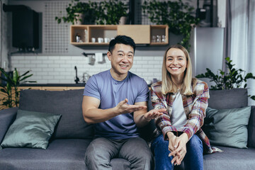 Video call of happy couple, woman introduces friends to husband, family happy at home on sofa