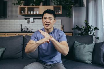 man talking on webcam, angry gesturing with hands, asian looking at camera, online call sitting on...