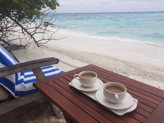 Two cups of coffee on a wooden table. Maldives, the white sand beach near the blue ocean.