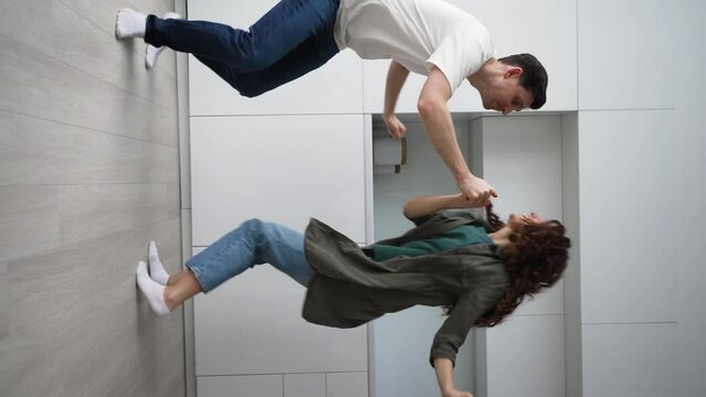Young cheerful couple dances together in jive style. Happy man and woman in casual clothes have fun against modern furniture at home. Vertical shot