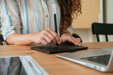 Close Up Photo of Woman Hands Drawing Something on a Graphic Tablet and Laptop Computer while Sitting at Home Office Desk