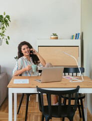 Happy Businesswoman Talking on a Mobile Phone at Home. 
Cheerful smiling business woman speaking on her phone while holding a cup of coffee and working on her laptop computer.