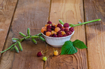 Raspberries in a white cup. On a wooden background with green leaves. A vase of red and white raspberries on boards. High quality photo