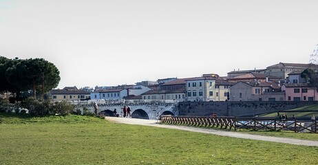 People enjoying the sun in the park near Tiberio bridge, from Roman times, in Rimini. Italy