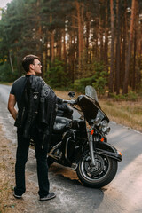 Selective focus of young man in black leather jacket standing near motorcycle