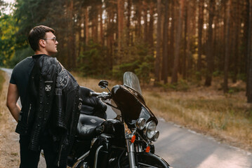 Fototapeta na wymiar Selective focus of young man in black leather jacket standing near motorcycle
