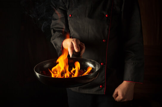 Professional chef cooking food in pan with fire flame on black background. Restaurant and hotel service concept. European cuisine. Vegetarian cuisine.