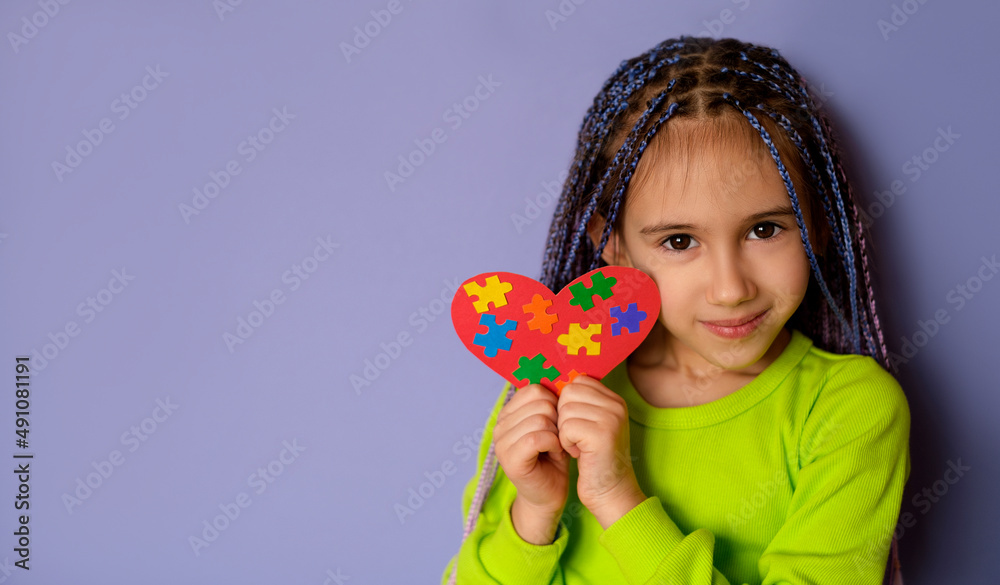 Wall mural a cute child is holding a heart-shaped card with colorful puzzles - a symbol of autism. support for 