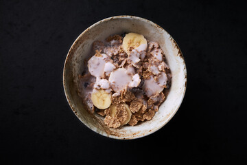 Bowl of granola with yogurt and banana. Concept for a tasty and healthy meal. Dark stone background. Top view. Close up. Copy space. 