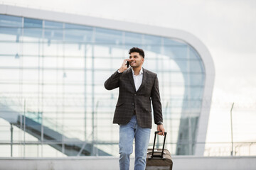 Portrait of young handsome Indian business man walking outside to station or airport talking on the...