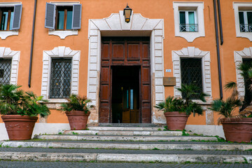 Fototapeta na wymiar Rome, Italy - 20.02.2022: Entrance to the orange building. Open doors and palm trees in clay pots on the steps
