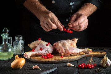 Professional chef prepares raw chicken legs in the restaurant kitchen. The cook puts the red viburnum on the chicken leg before baking. Grande cuisine