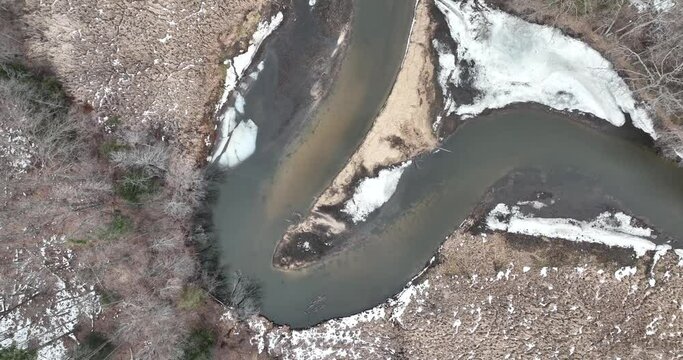 Beautiful frozen river with snow, ice, and flowing water. Clear water with riverbed. Following the flow of the river. Drone Footage.