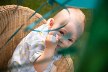 Little boy blond European German age one 1 year old sits in a rattan chair and points with a finger for his birthday